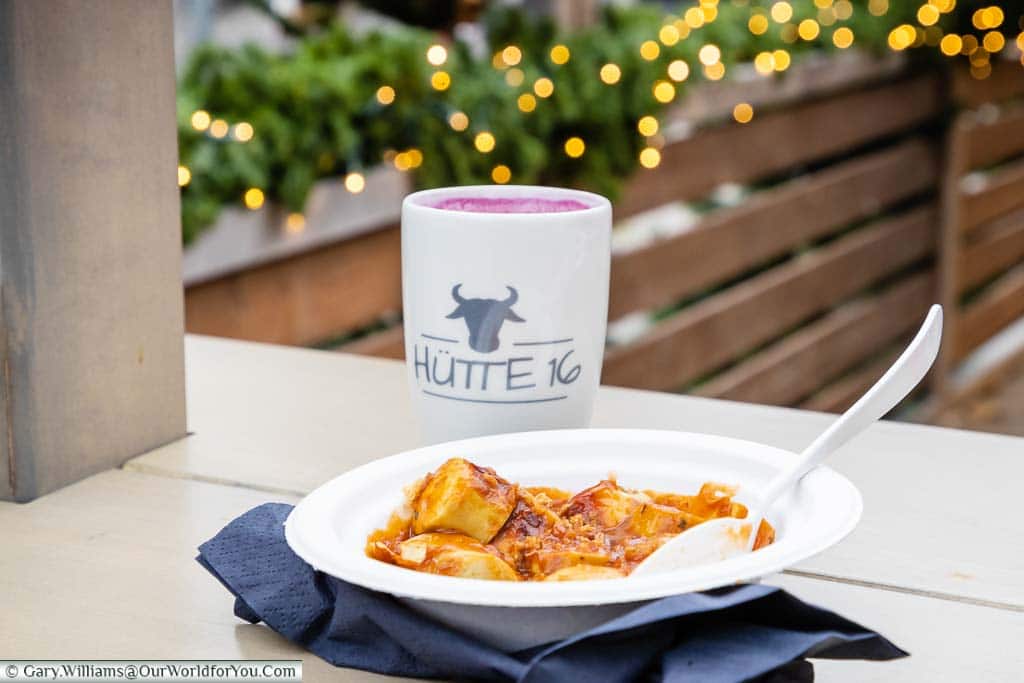 A paper plate filled with Currywurst, with a mug of Glühwein in the background, from Hutte 16
