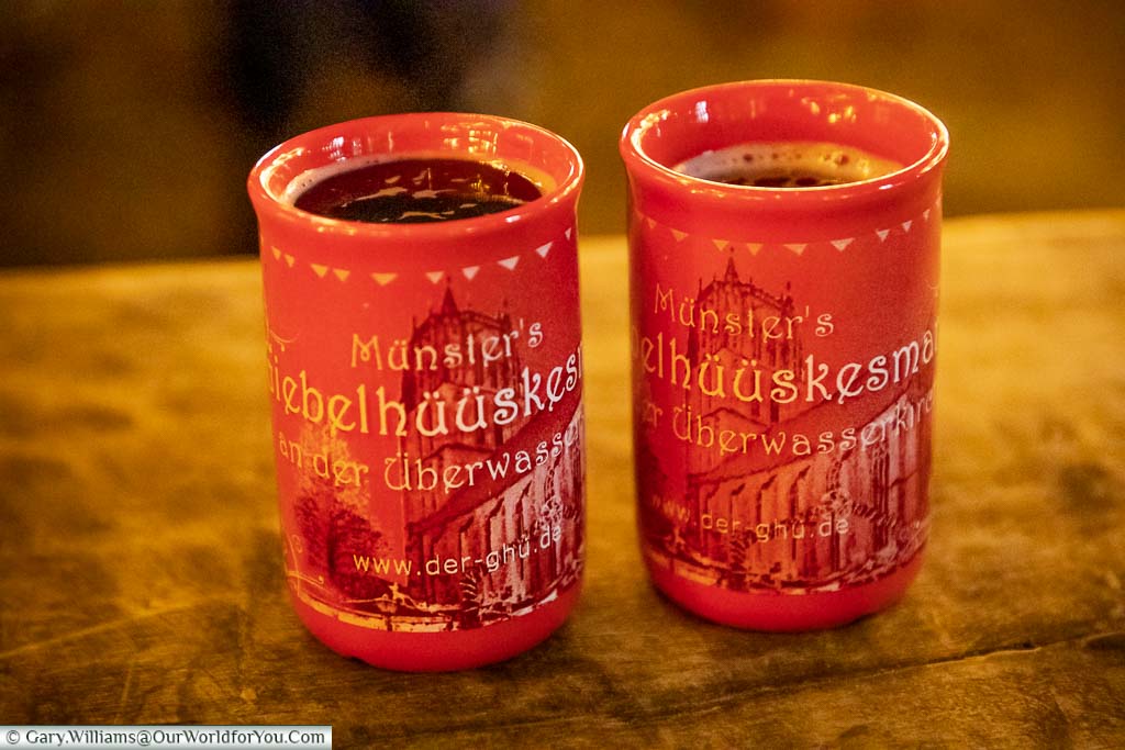 Two mugs of Giebelhüüskesmarkt glühwein on a wooden table in Münster Christmas Markets