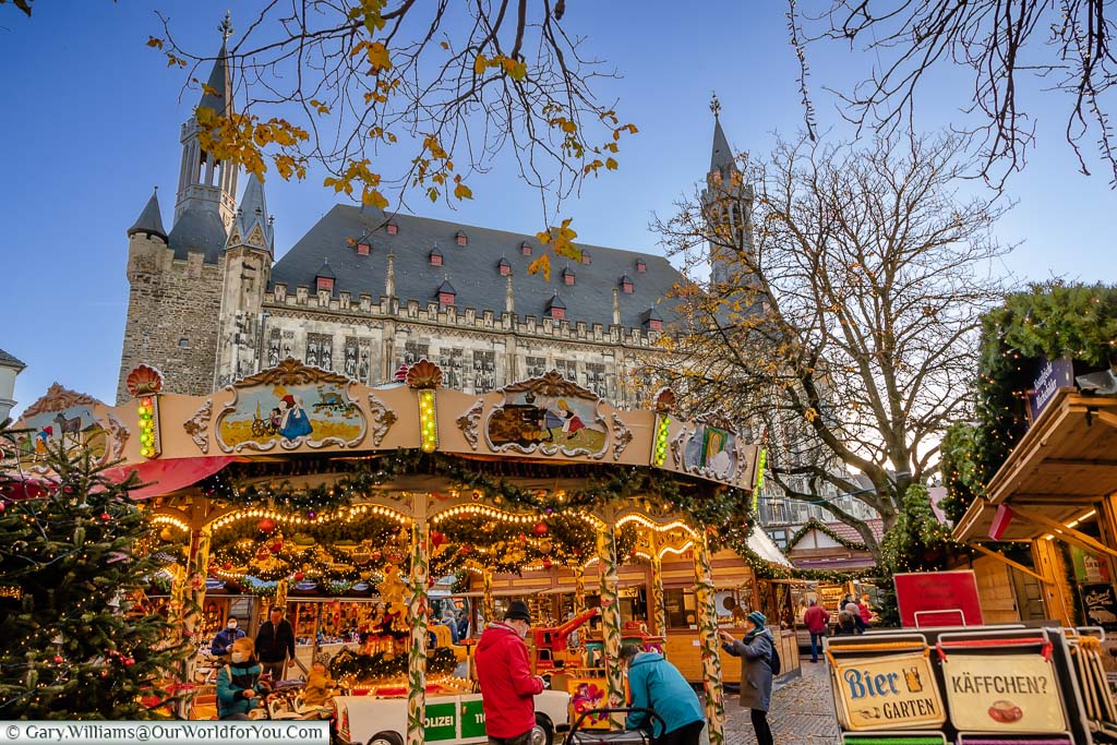 A traditional carousel in Aachen's Christmas market with the Gothic Rathaus in the background at dusk