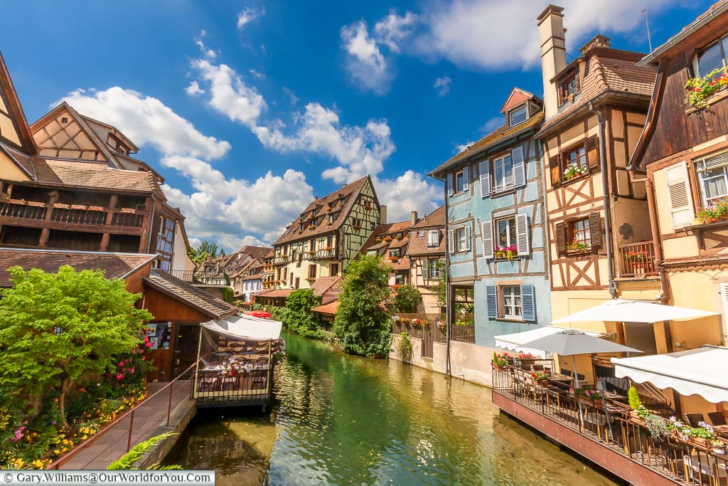 Restaurants at the base of brightly coloured, half-timbered buildings lining the canal in Colmar, France