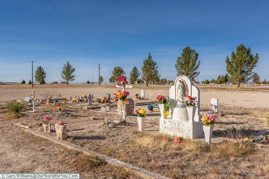 A collection of graves, all decorated with vibrant bouquets in the corner of a cemetery in Marathon, Texas, USA