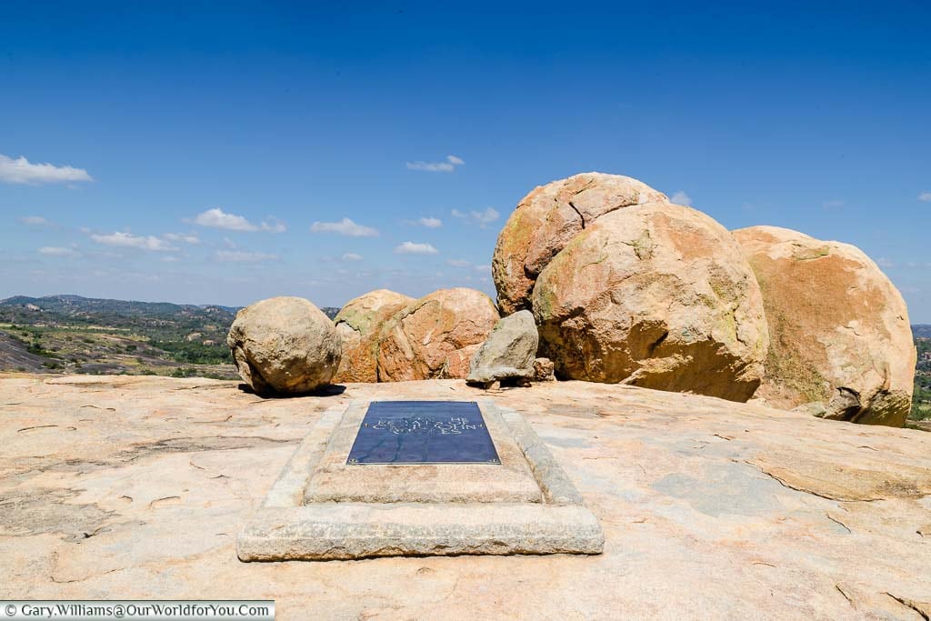 A full-size plaque over a stone marking the last resting place of Cecil John Rhodes on top of World's View in front of a collection of boulders.