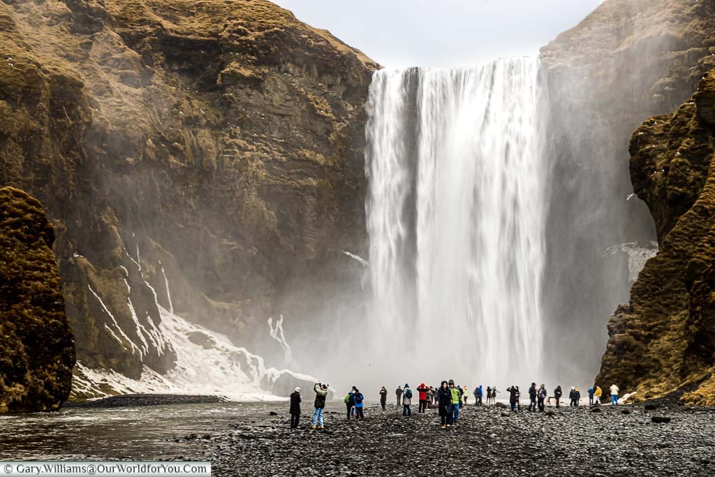 People gathering in front of the Skógafoss waterfall as seen from a distance