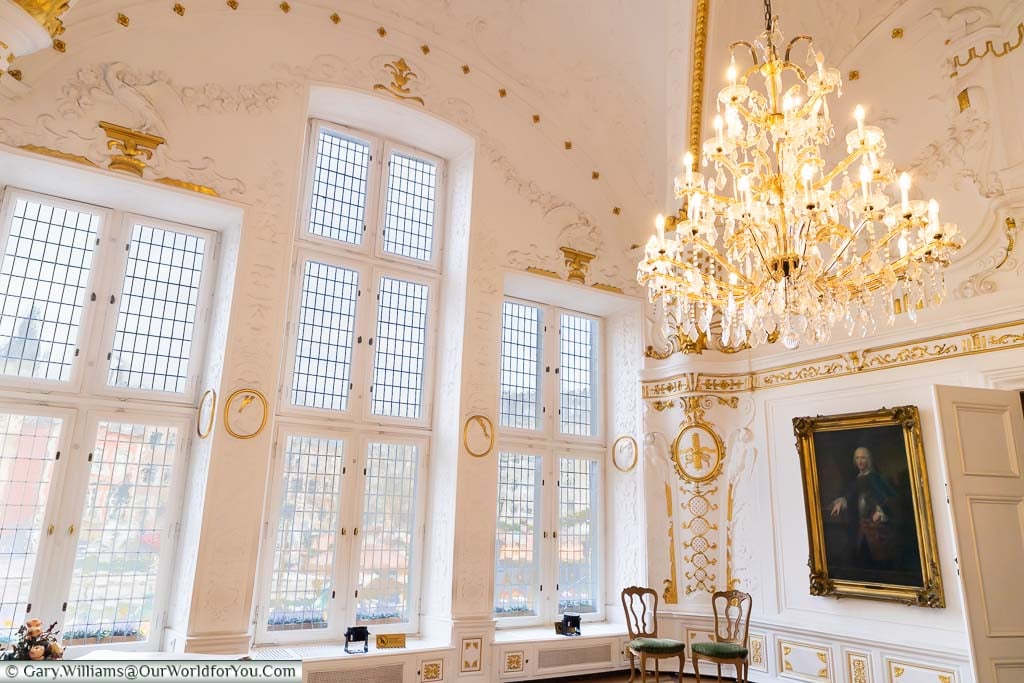 The White Hall inside Aachen's Rathaus is painted white with gold embellishments, an ornate period chandelier and views out onto the square in front of the town hall.