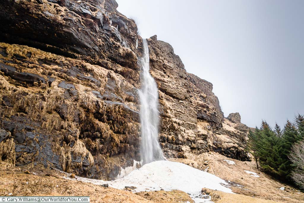 A long narrow waterfall tumbling down a rockface into the last remaining snow of the season