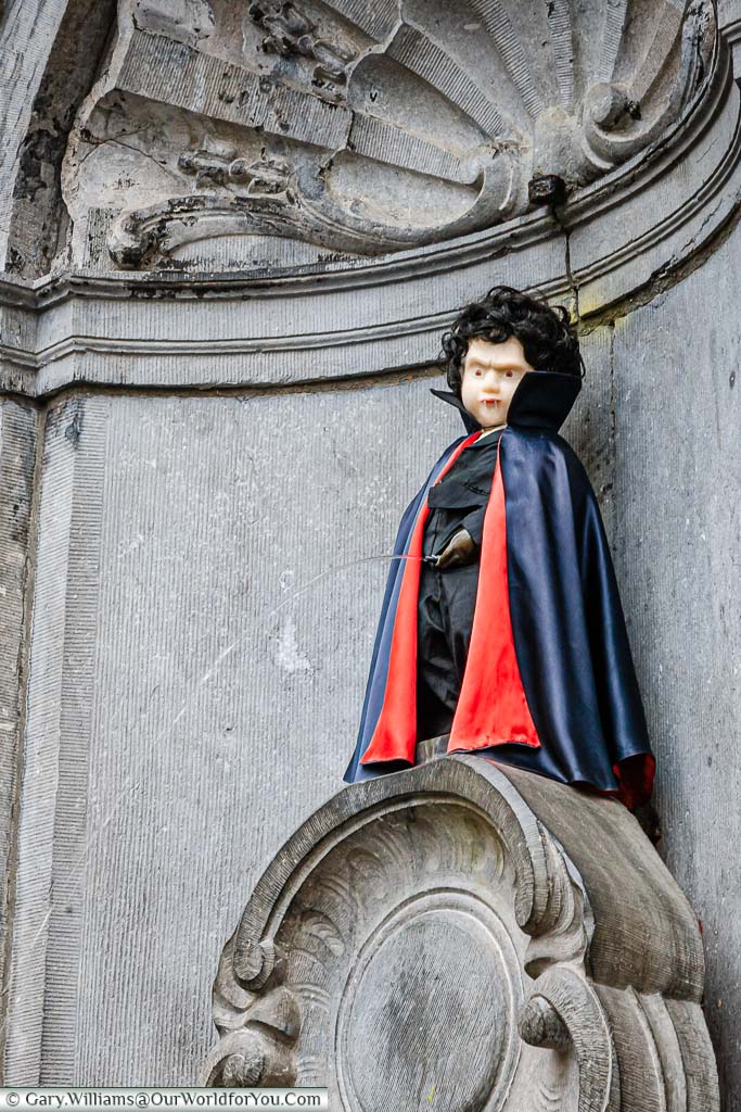 The Manneken Pis statue in Brussels dressed as a vampire with a fanged mask and a red-lined deep blue cape