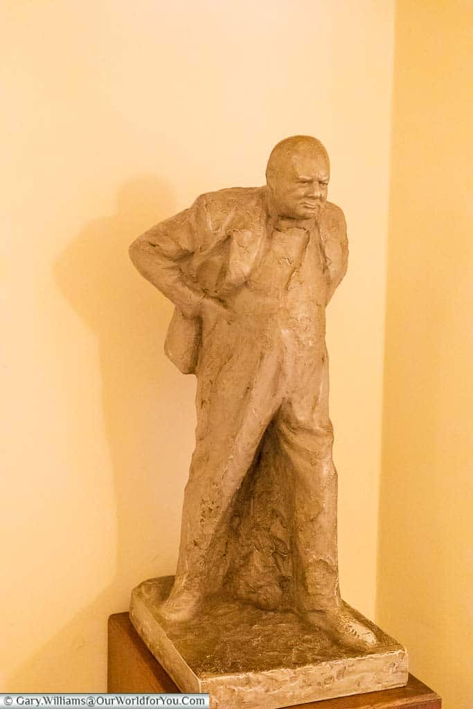 A small cream stone statue of Sir Winston Churchill thrusting forward with his hands on his hips.