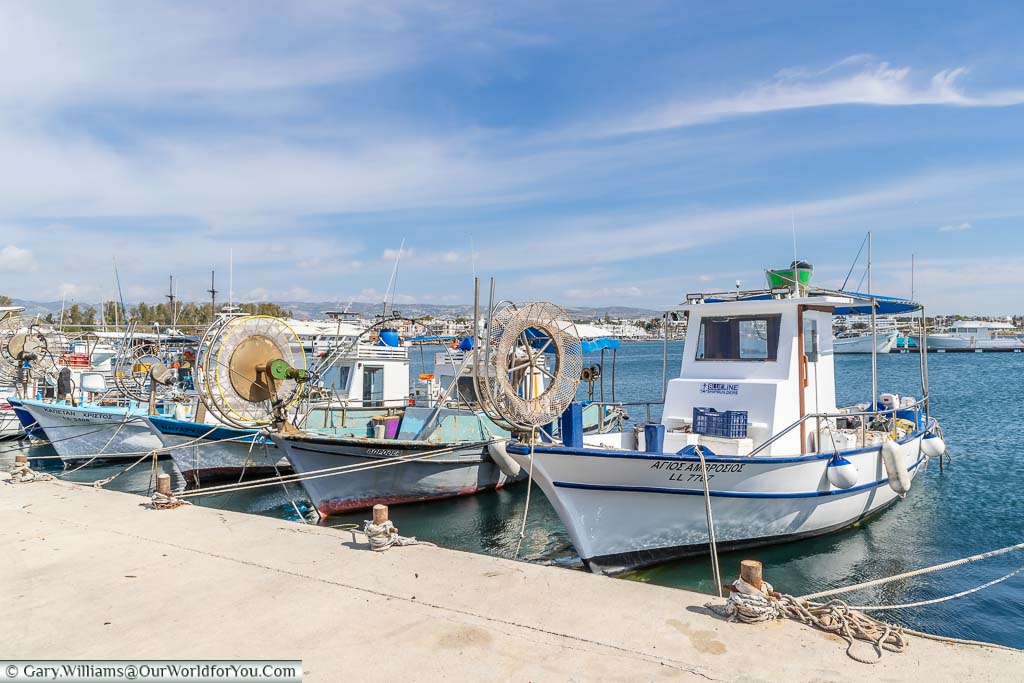 A row of small fishing boats lined up in Paphos harbour on a bright day under blue skies.