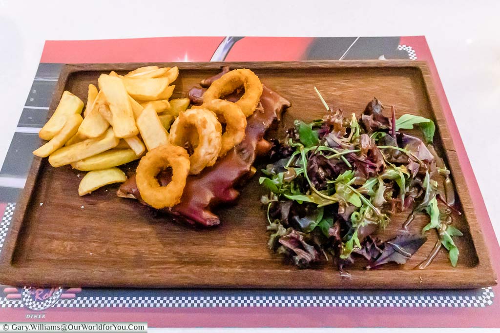 Ribs, topped with onion rings, chunky fries and a salad served on a wooden board at the Rock 'n' Roll diner at tge Olympic Lagoon Resort Paphos