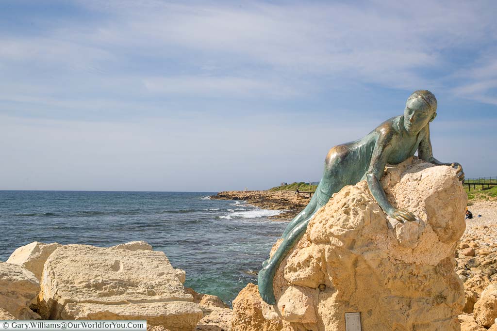 A bronze statue of a woman, named Sol Alter, draped over a rock in Pathos harbour