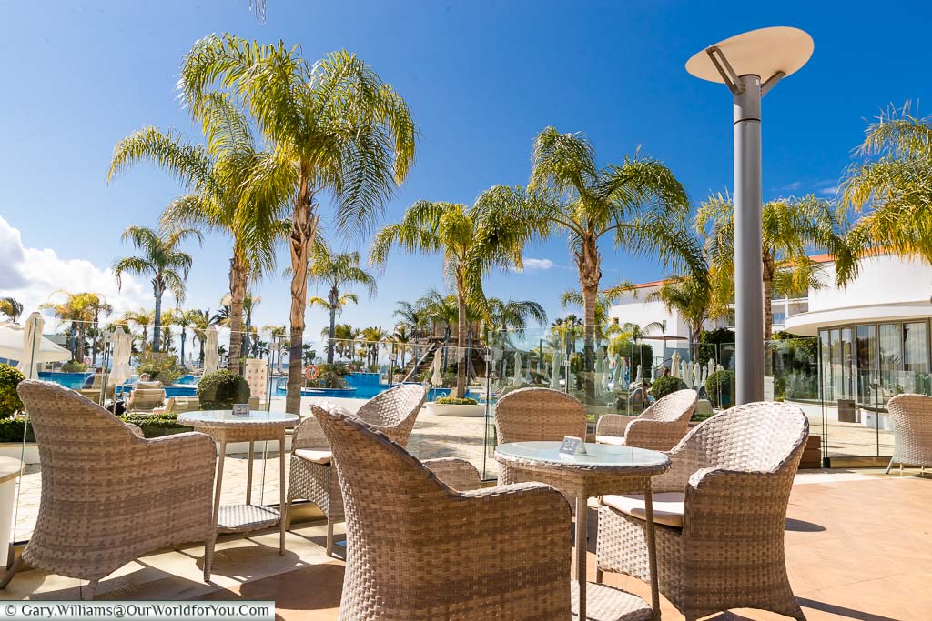The wicker chairs lining the Terrace, overlooking the poolside on a bright day at the Olympic Lagoon Resort Paphos
