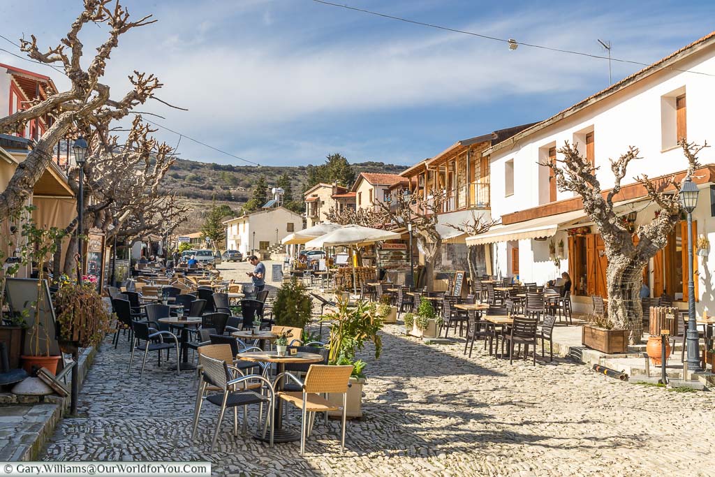 Tables & chairs set outside restaurants on a cobbled street in Omodos wine village in the Cypriot hills
