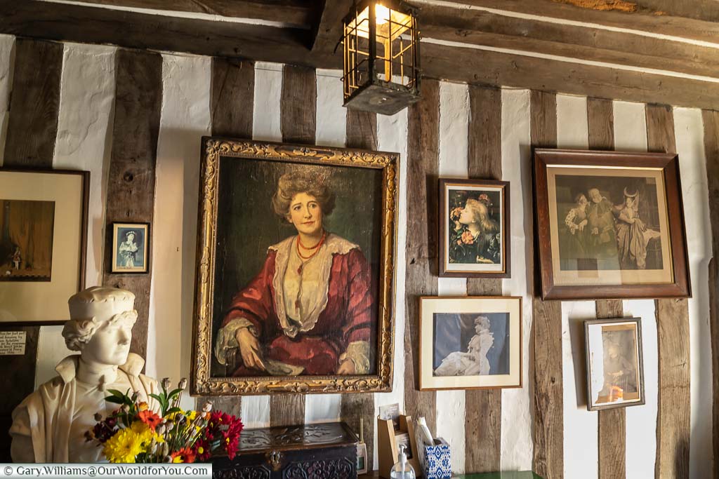 An oil portrait of Dame Ellen Terry in a red dress hanging on a half-timbered wall within Smallhythe Place in Kent