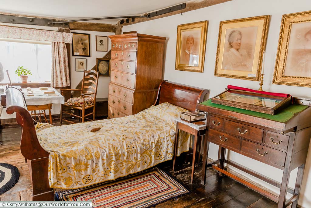 A single sleigh bed in Dame Ellen Terry’s bedroom next to a large chest of drawers and family portraits on the walls.