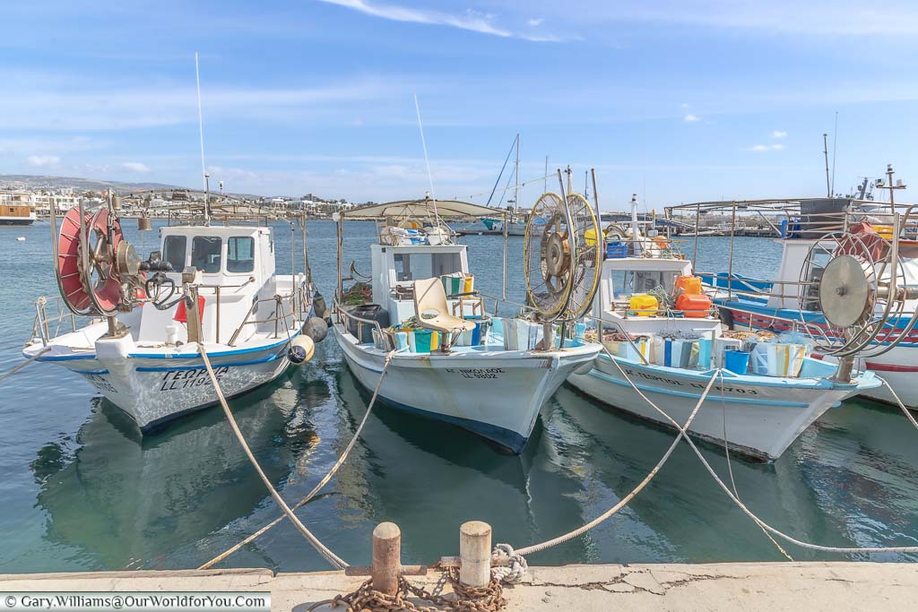 A row of small fishing boats lined up in Paphos harbour on a bright day under blue skies.