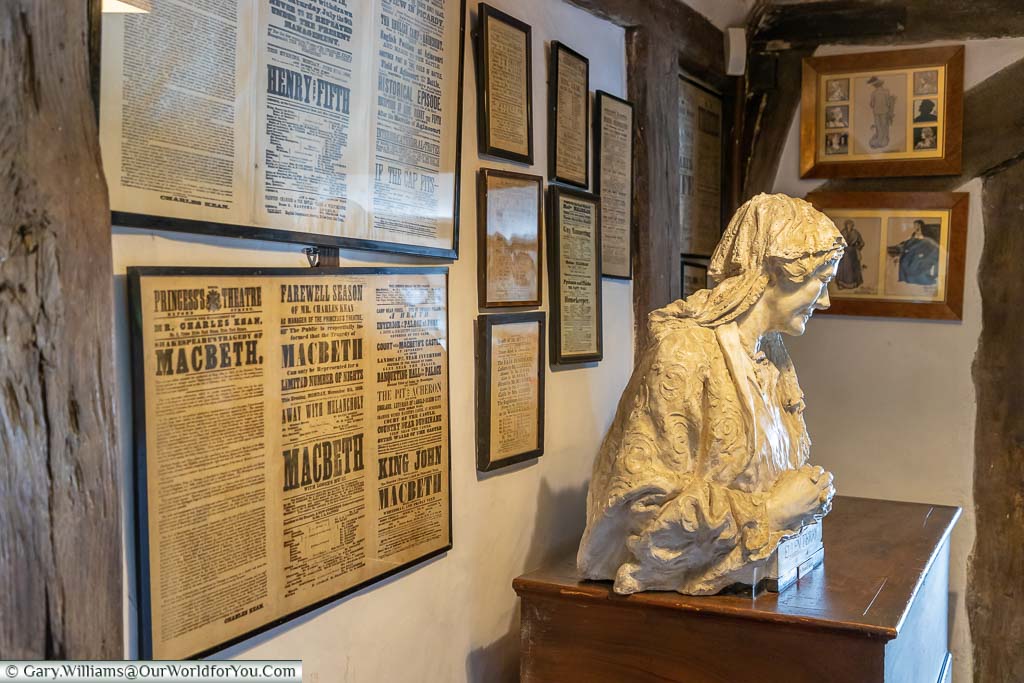 Framed press cuttings of reviews of Ellen Terry’s performances on a wall behind a bust of the actress.