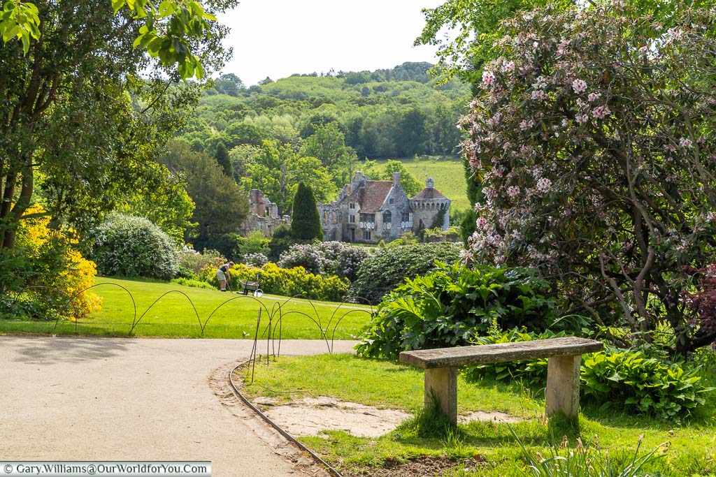A bench next to a path leading down through the gardens to old Scotney Castle in the distance