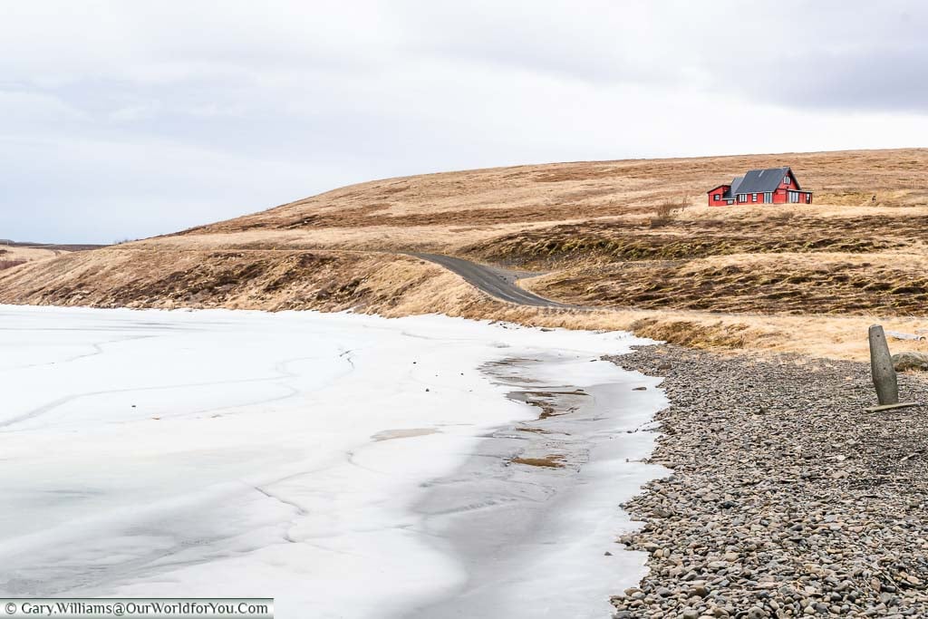 A lone red wooden lodge at the edge of the frozen lake of Vesturhopsvatn in northwest Iceland