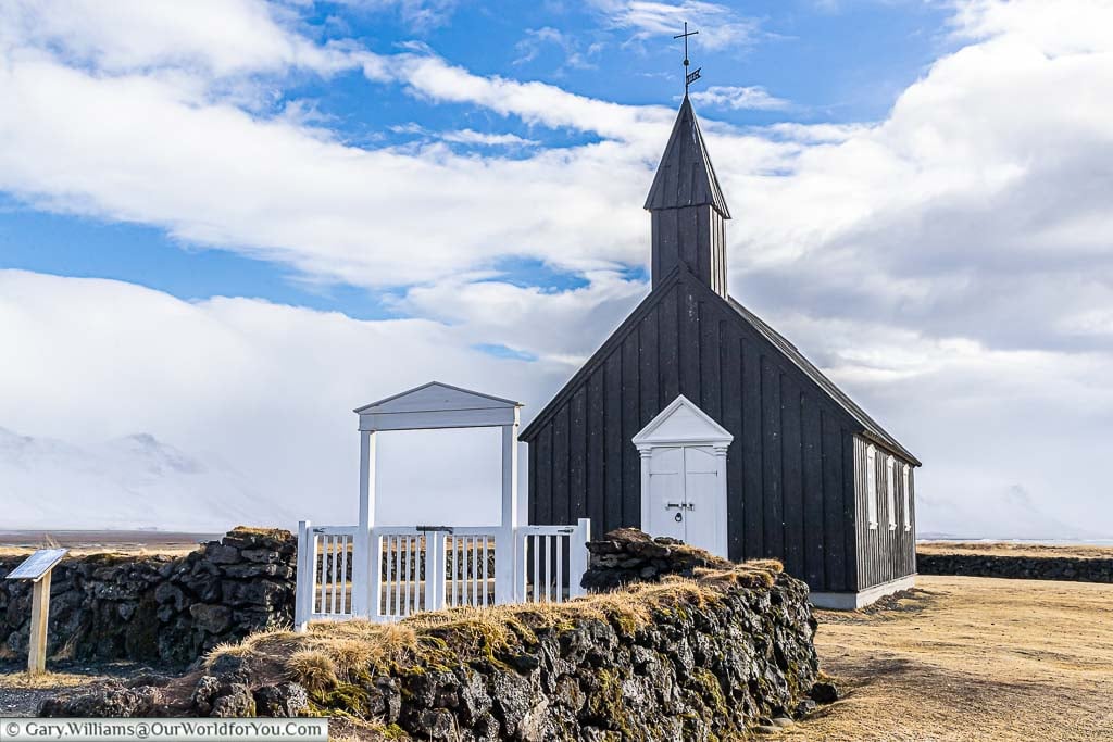 The simple Black wooden church - Búðakirkja - on the western side of Iceland, under blue cloudy skies.