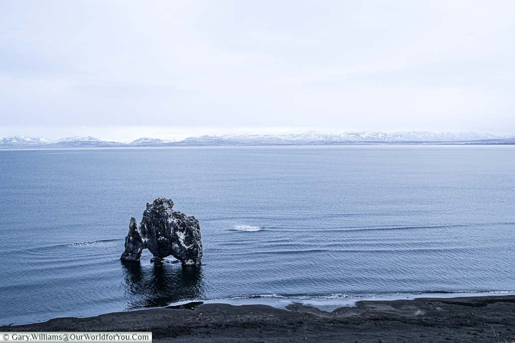 A wide shot of the rock formation known as Hvitserkur, said to resemble a dragon drinking from the lake in Northern Iceland.
