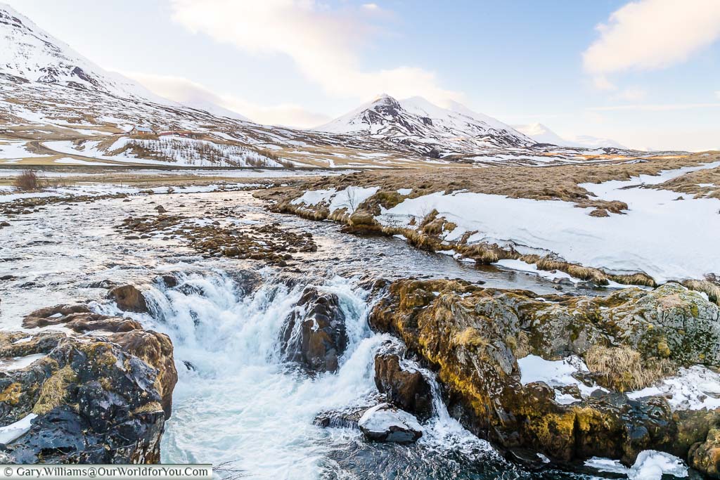White water on a stream just off route one in Northern Iceland outside Akureyri against a backdrop of mountains.