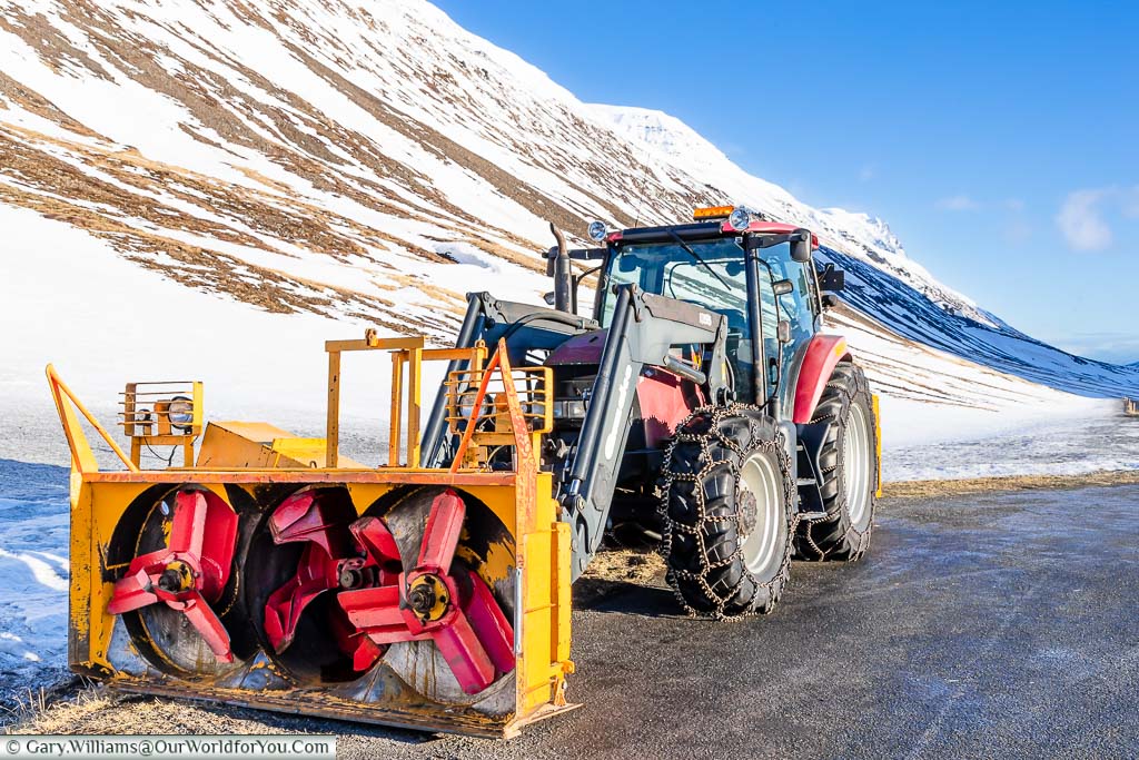 A tractor fitted with snow chains and three snow cutting blades in a layby on Route one in Northern Iceland.