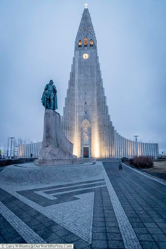 The Hallgrímskirkja church in Reykjavik, Iceland at dusk. In front of it stands a statue of the Viking Leifur Eiríksson.