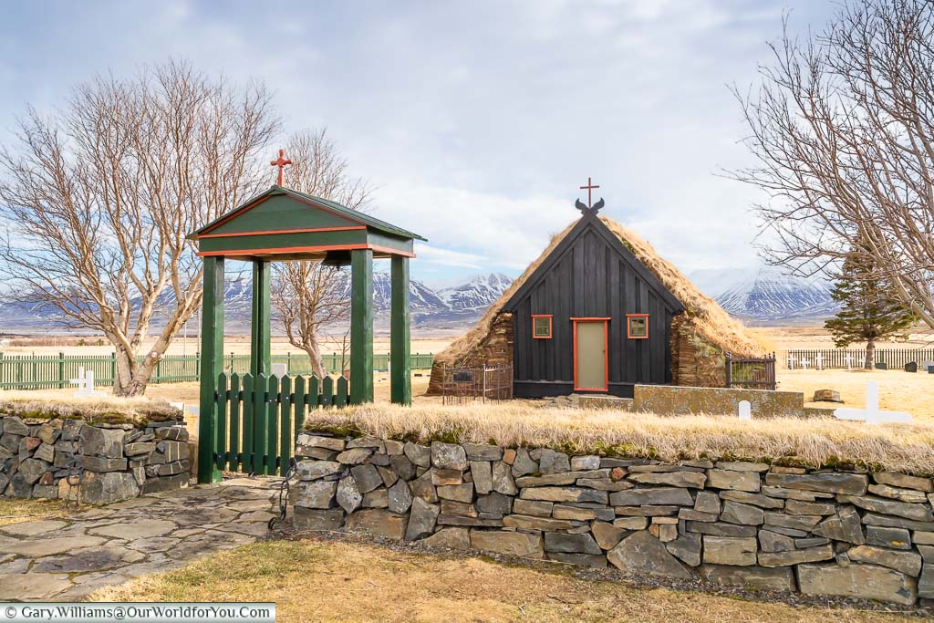 A green wooden lychgate in front of the wooden Víðimýrarkirkja church with its turfed roof in northwest Iceland