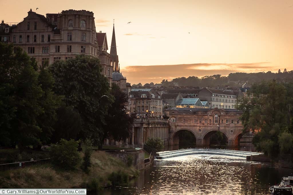 The view over the River Avon towards the weir in front of the Pulteney Bridge in Bath at dusk