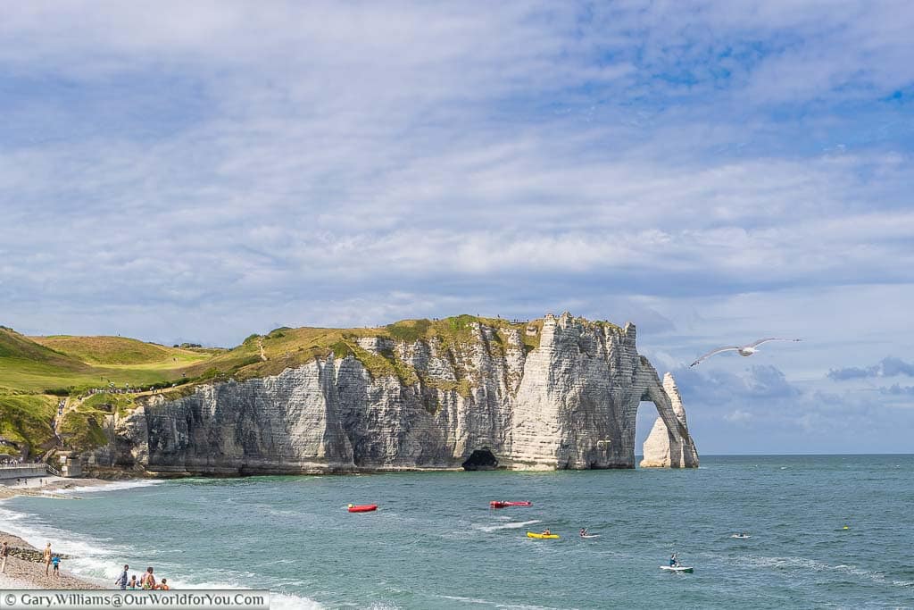 A beach view of Étretat's shoreline, including its white cliffs and legendary arch formation.