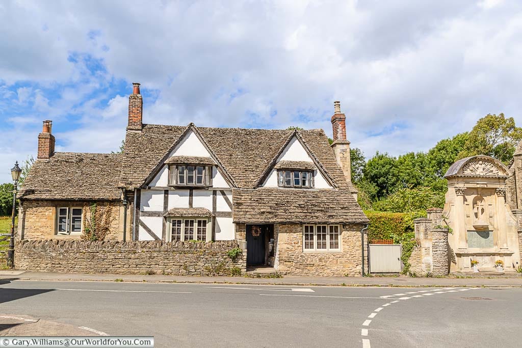 A 17th-century timber-frame and rubble stone house with stone slate roof next to the World ward One War memorial in Lacock, Wiltshire.