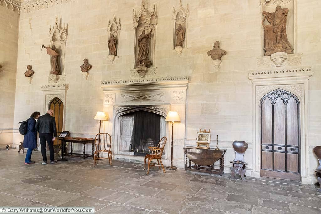 A large fireplace set in a stone wall surrounded by statues and busts set in nooks in the Great Hall of Lacock Abbey