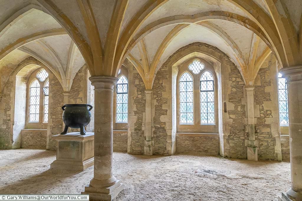 The vaulted ceiling of the warming room at Lacock Abbey with a large iron cauldron resting on a plinth.