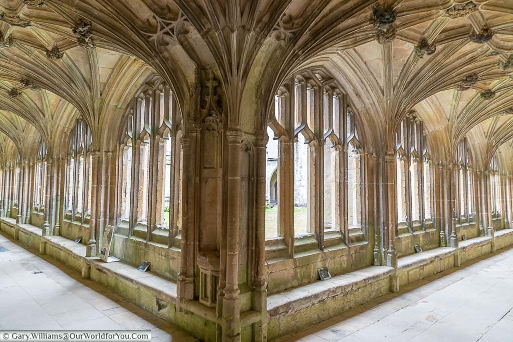 The corner of the cloisters in Lacock Abbey with its ornate fan arches and stone windows onto a central courtyard