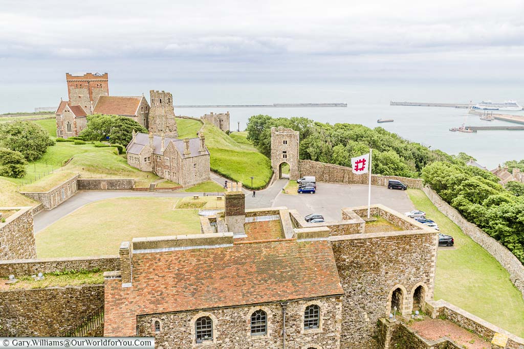 The view from the top of Dover Castle's Norman keep, surrounded by stone walls and a Roman Lighthouse & historic church in foreground, to the harbour beyond.