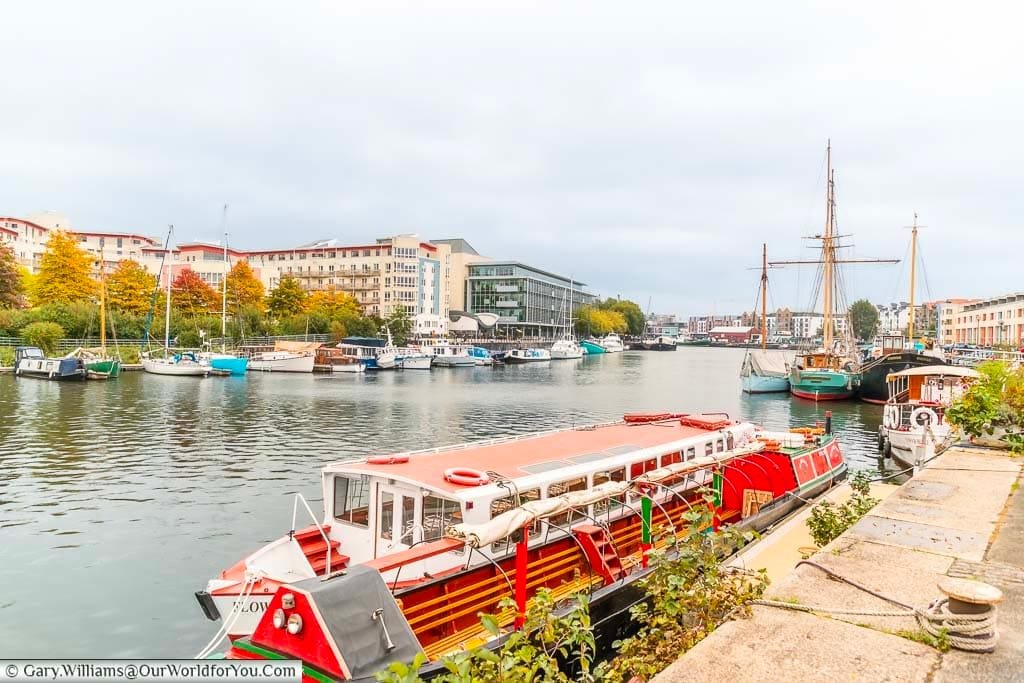 The view from Bristol's Harbourside Walk, looking back along the harbour with various boats & ships of all shapes and sizes moored up