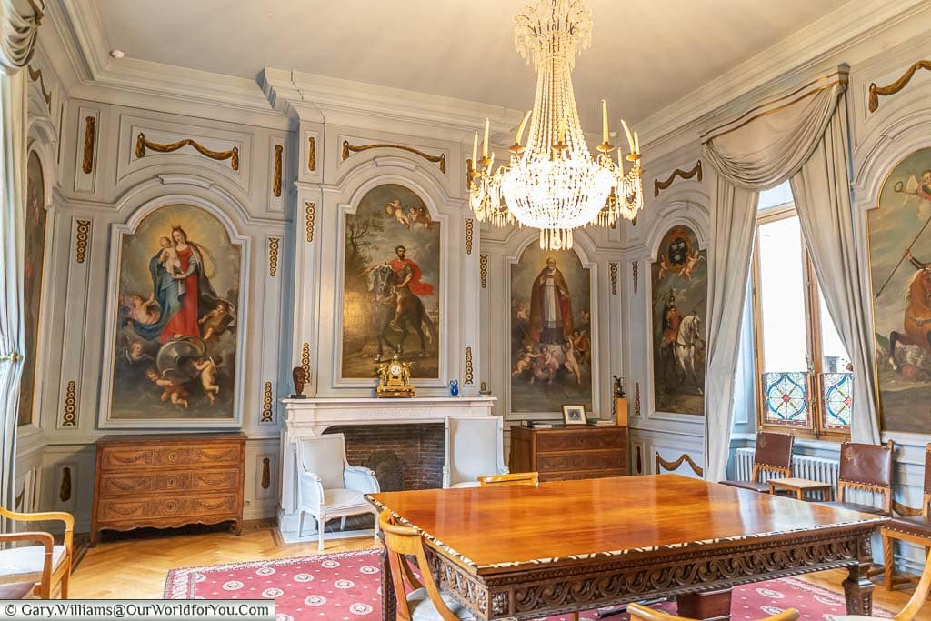 A chandelier hangs from an ornate reception room in a pale blue with classic images painted in panels in Leuven's town hall