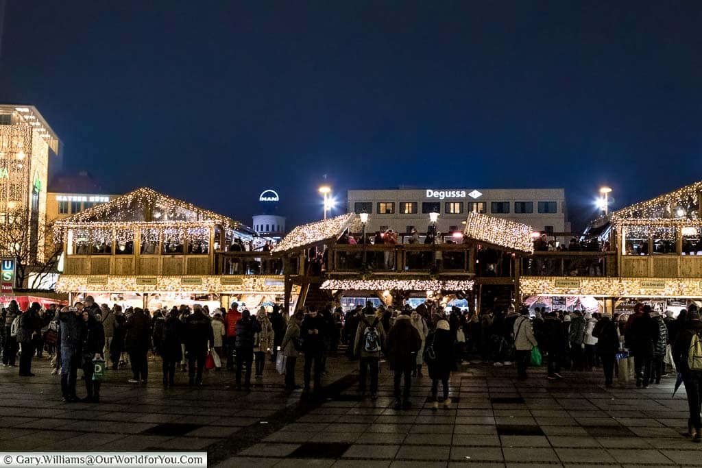 Groups of people gather in front of the Christmas markets stalls that line the edges of the ice rink in Karlsplatz.
