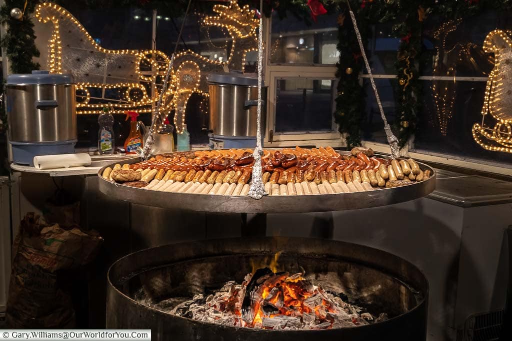 An open grill full of sausages cooking above a charcoal fire set in a steel container below on a Christmas Market stall in düsseldorf, germany