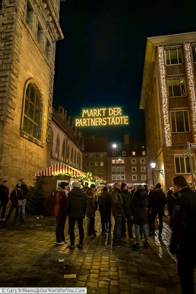 Groups gathering under an illuminated sign to the Markt der Partnerstadte, part of nuremberg's christmas markets