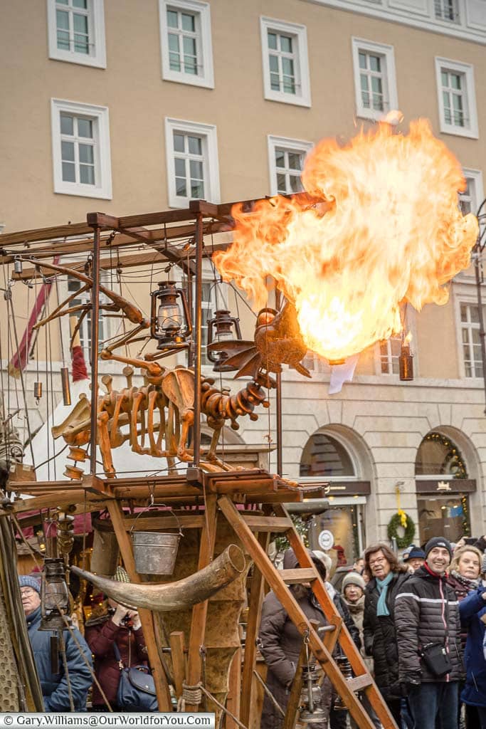 A mobile performance piece of a dragon skeleton puppet breathing flames as the crowds watch on.