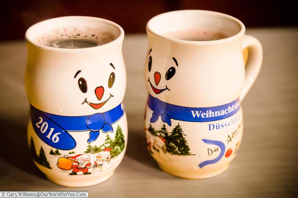 Two mugs of steaming glühwein with a snowmen design on the Düsseldorf Christmas Markets.