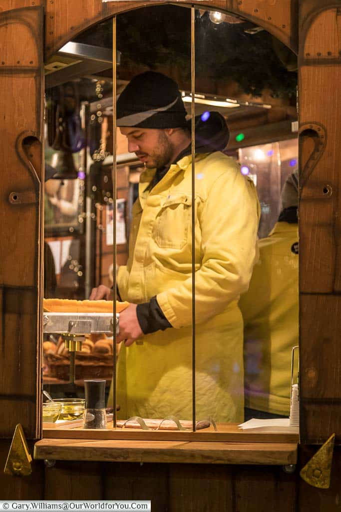 A christmas market trader preparing grilled raclette cheese for a customer at düsseldorf christmas markets