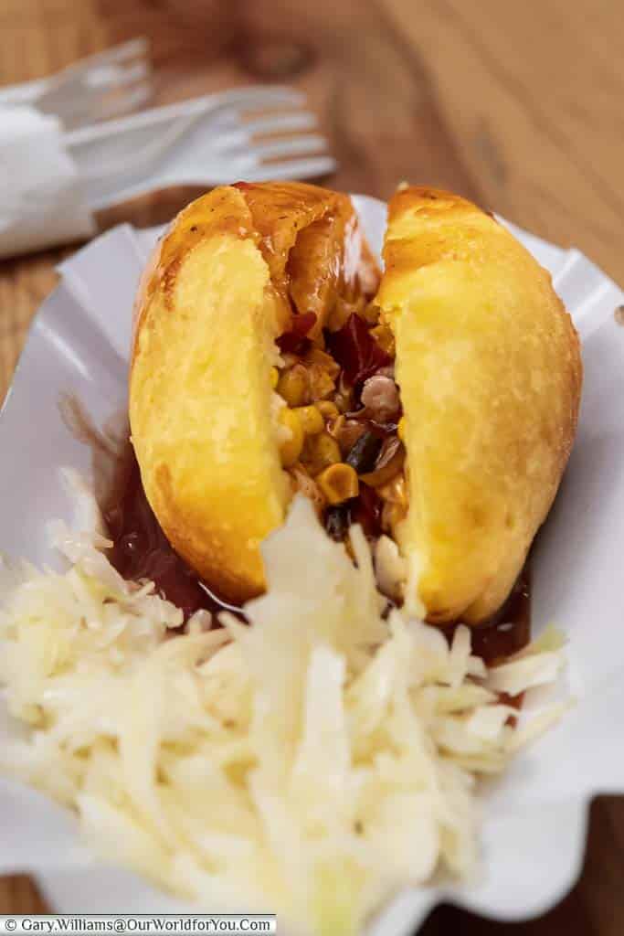 A golden hot potato filled with meat mixture and a deep brown sauce, served with a side serving of coleslaw on düsseldorf's christmas markets
