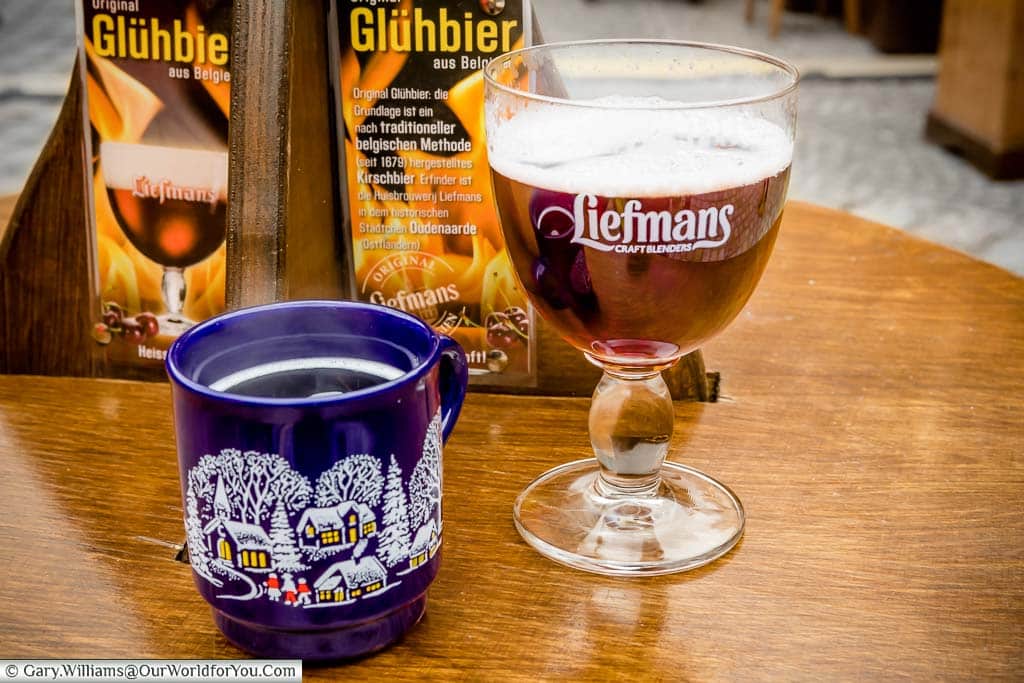 A mug of glühwein, and a chalice-shaped glass with a glühbier, or hot, spice, beer on a wooden barrel in the Residence Christmas market.