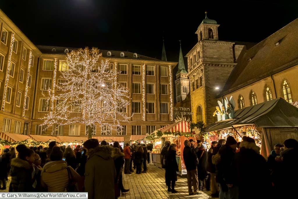 Groups gathering around huts in the Markt der Partnerstadte at night, part of nuremberg's christmas markets