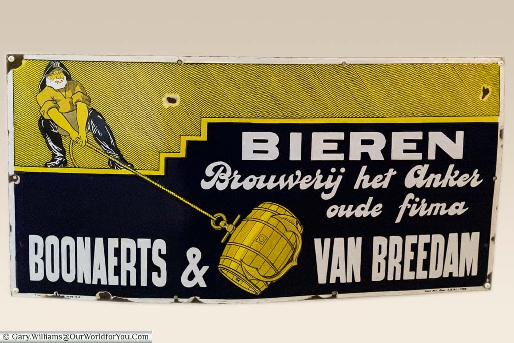 An old advertising sign for het anker beers featuring a sailor hoisting a beer barrel up using an anchor.