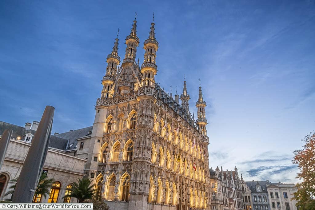 Leuven's historic City hall is illuminated under the blue sky at dusk.