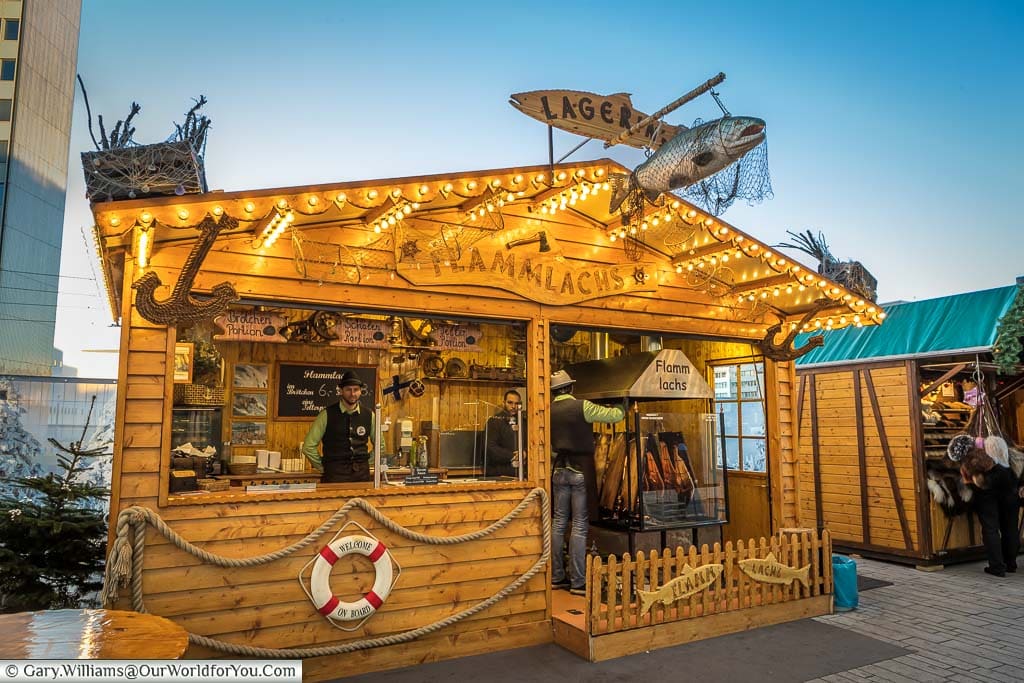A large wooden cabin at one of the Düsseldorf Christmas Markets selling salmon-filled rolls from sides of salmon cooked over wood on-site.