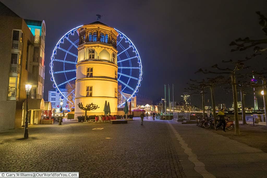 A lit five-storey historic tower than now acts as a museum, with the large Ferris-wheel, named Wheel of Vision, in the background.